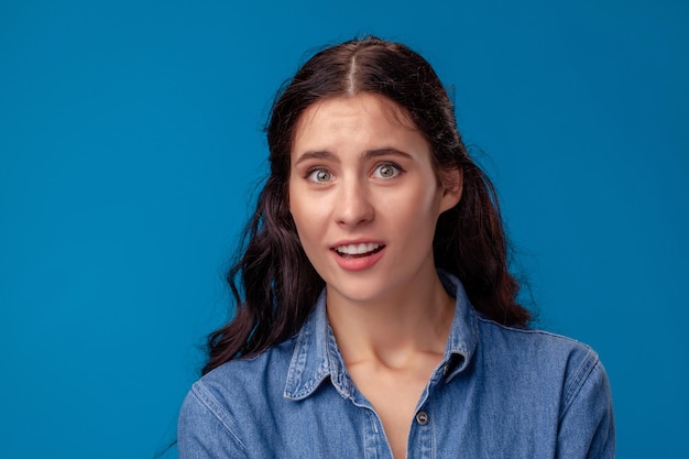 Close-up portret van een aantrekkelijke brunette meisje met lang krullend haar poseren op een blauwe achtergrond.