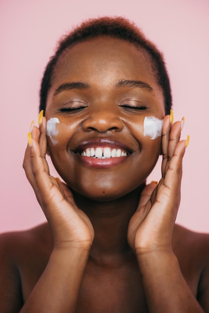 Close-up portret van een Afro-Amerikaanse vrouw die hydratatie crème toepast op haar lachende gezicht geïsoleerd ...