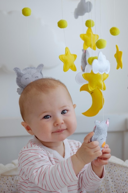 Foto close-up portret van een baby in de wieg zitten en kijken naar de camera, spelen met speelgoed van wieg mobiel.