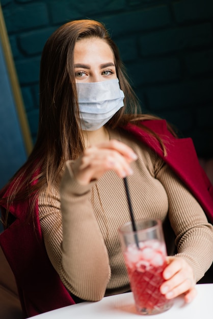 Close-up portret van een blanke vrouw die een medisch masker draagt en in de straat staat tegen de achtergrond van een café