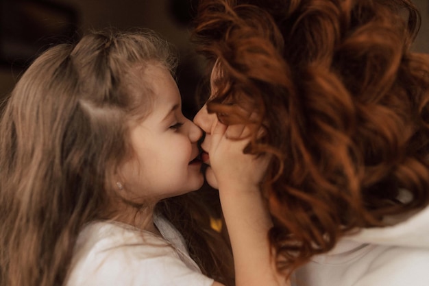 Foto close-up portret van een charmant meisje kust haar moeder jonge vrouw met rood krullend haar kust haar dochtertje
