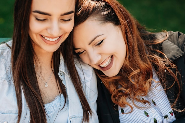 Close-up portret van een charmante plus size vrouwen met lang rood krullend haar lachen terwijl ze haar hoofd leunt op haar vriendin die ook buiten lacht.