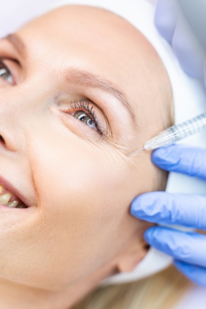 Close-up portret van een glimlachende dame die een hyaluronzuurinjectie krijgt in een schoonheidssalon
