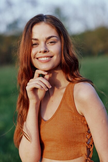 Close-up portret van een glimlachende jonge vrouw in de zon met rood haar in de natuur