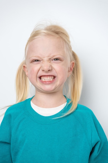 Close-up portret van een klein meisje met blond haar dat glimlacht en tanden laat zien op een witte achtergrond