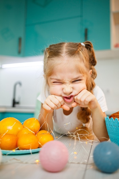 Close-up portret van een klein meisje van zeven jaar oud. Lekker gek doen aan de tafel in de keuken. Gekleed in een wit t-shirt