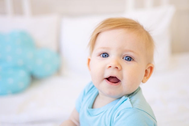 Close-up portret van een kleine blonde baby lachende baby met blauwe ogen thuis op het bed