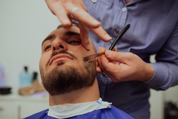 Close-up portret van een knappe jonge man die baard scheert met een scheermes