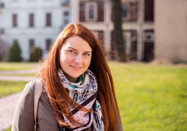 Close-up portret van een lachende jonge roodharige meisje met lang haar camera kijken terwijl buitenshuis staan, lentetijd