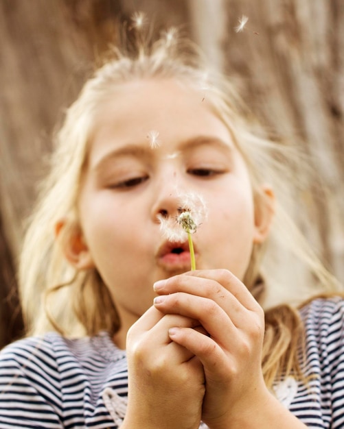 Close-up portret van een meisje dat paardenbloem blaast