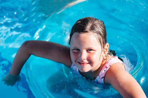 Close-up portret van een meisje in een roze zwembroek drijvend in een transparante opblaasbare cirkel in de...