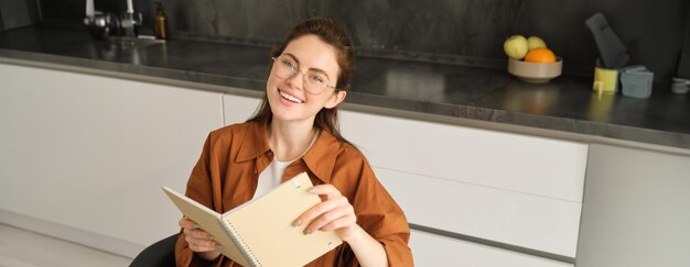 Close-up portret van een mooie jonge vrouw met een notitieboek lezen planner zitten thuis en