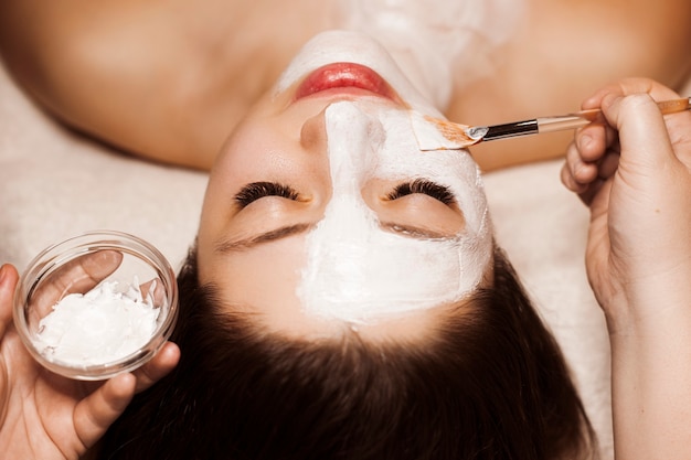 Close-up portret van een mooie vrouw doet een routine wit masker huidverzorging in een kuuroord.