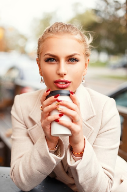 Close-up portret van een mooie vrouw met koffie in een stijlvolle jas op straat