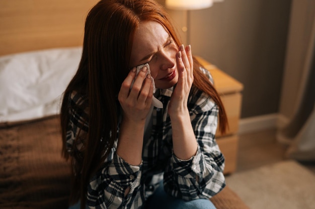 Close-up portret van een ongelukkige depressieve roodharige vrouw die huilt en tranen afveegt met papieren zakdoekjes lijdt aan verdriet, echtscheiding of maakt het uit met vriendje