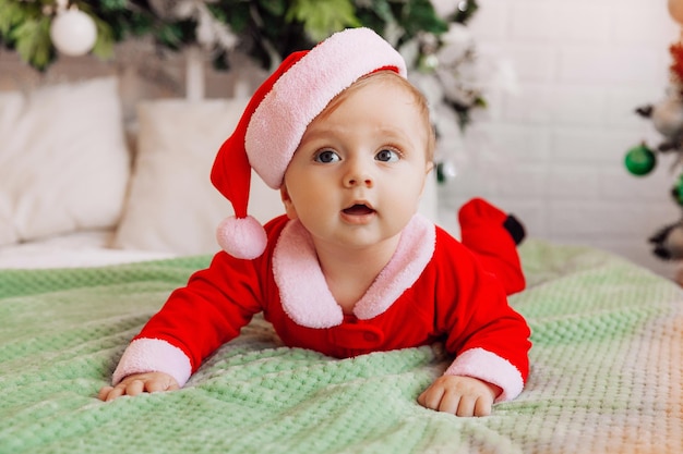 Close-up portret van een pasgeborene. Kaukasische baby 6 maanden in een kerstmanpak liggend op een gebreide gezellige deken op het bed. Kerst 2022
