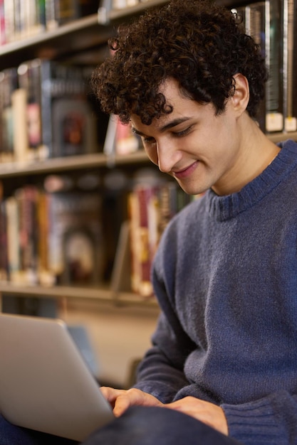 Close-up portret van een slimme zelfverzekerde positieve mannelijke student die laptop gebruikt voor studie op de bibliotheekcampus