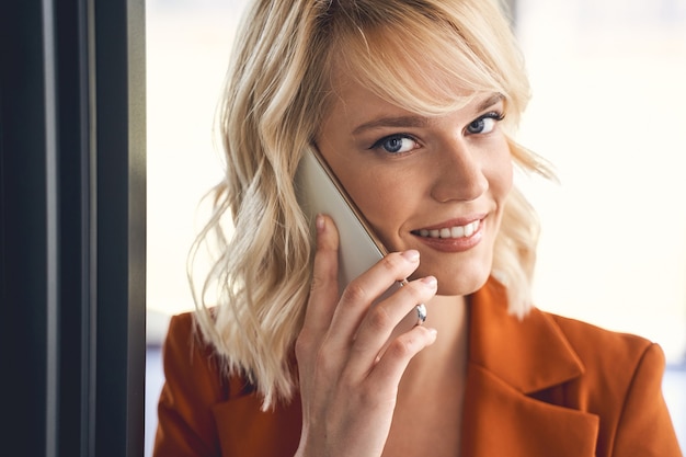 Close-up portret van een tevreden mooie jonge zakenvrouw die binnenshuis op een mobiele telefoon praat