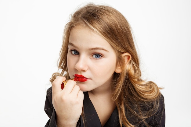 Close-up portret van een vrolijk kind dat het goedmaakt, het gedrag van de moeder kopieert. Lippenstift opdoen, recht kijken.