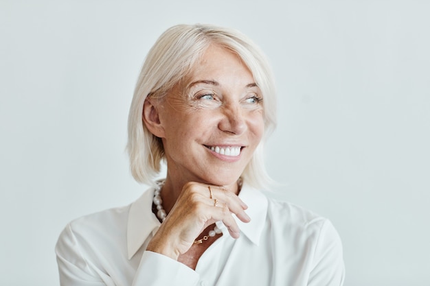 Close-up portret van elegante volwassen vrouw die wegkijkt en lacht tegen een witte achtergrond, kopieer ruimte