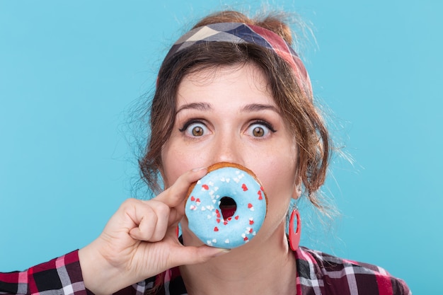 Close-up portret van geamuseerde grappige jonge mooie vrouw met donut in de buurt van de mond die zich voordeed op een blauw