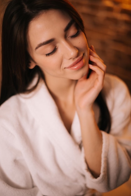 Close-up portret van gezicht van mooie jonge vrouw in witte badjas met gesloten ogen op achtergrond van bakstenen muur. concept van luxe professionele massage.