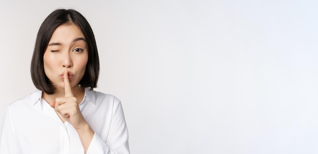 Close-up portret van jonge aziatische vrouw die zwijg maakt shhh zwijg teken druk met de vinger naar de lippen, spreek niet stil gebaar witte achtergrond