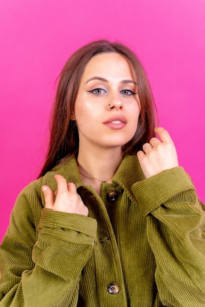 Close-up portret van jonge blanke vrouw in groene trenchcoat geïsoleerd op roze achtergrond camera kijken