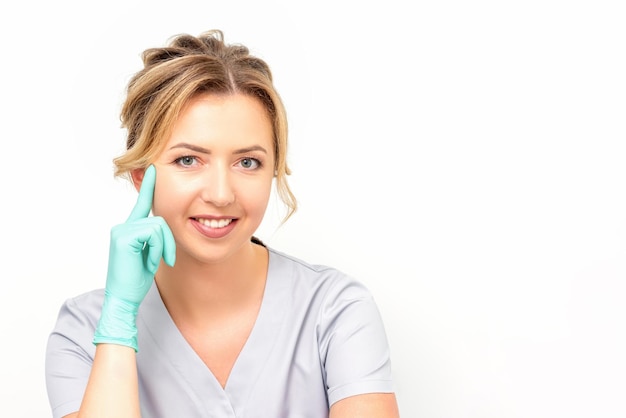 Close-up portret van jonge glimlachende vrouwelijke blanke gezondheidswerker die staat en naar de camera staart met handschoenen op witte achtergrond