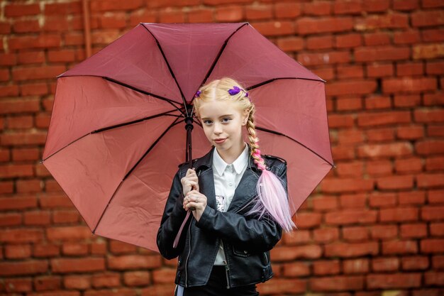 Close-up portret van kleine mooie stijlvolle jongen meisje met een paraplu in de regen in de buurt van rode bakstenen muur als achtergrond