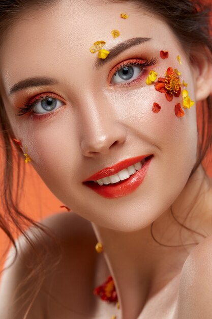 Close-up portret van mooi meisje met oranje make-up en bloemen op haar gezicht op zoek naar de camera