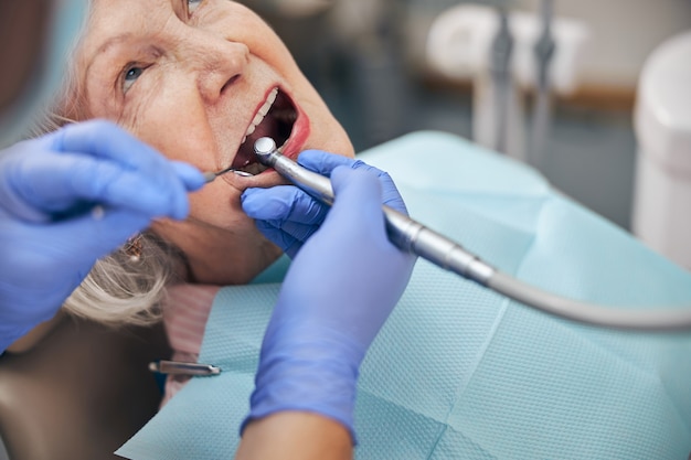 Close-up portret van patiënt zittend op de tandartsstoel terwijl tandarts bij procedure met tandheelkundige boor in moderne tandheelkundige kliniek