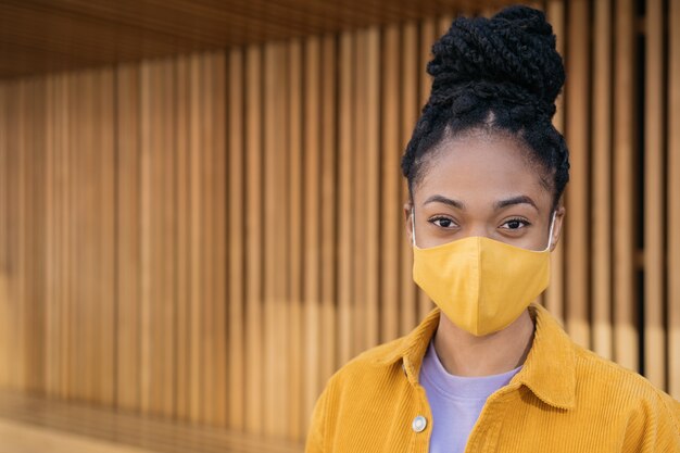 Close-up portret van peinzende Afro-Amerikaanse vrouw die een beschermend gezichtsmasker draagt en naar de camera kijkt