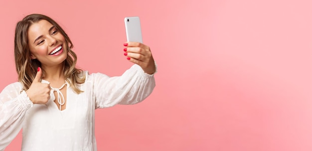 Close-up portret van stijlvolle mooie beauty blogger video opnemen op smartphone selfie te nemen met thumbsup op mobiele telefoon camera glimlachend blij aanbevelen plaats aan volgers