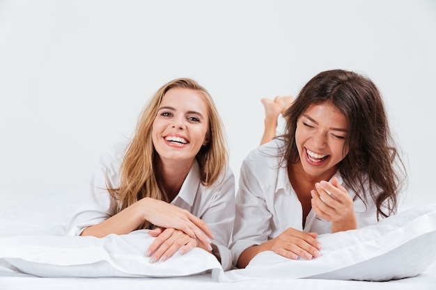 Close-up portret van twee lachende mooie vrouw die samen op bed ligt met witte lakens