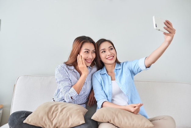 Close-up portret van twee opgewonden vriendinnen met mobiele telefoons, lachen. Gelukkige vrolijke vriendinnen die thuis rusten, genieten van gesprekken, plezier maken.