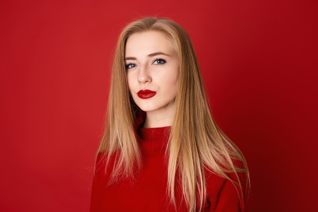 Close-up portret van verleidelijke blonde vrouw tegen een rode achtergrond