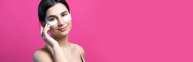 Close-up portret van vrij aantrekkelijk meisje met blote schouders met behulp van patches onder de ogen permanent over roze achtergrond