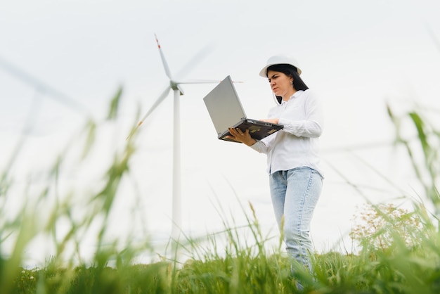 Close-up portret van vrouwelijke ingenieur in helm staan en het gebruik van laptopcomputer tijdens het controleren van het werk van windmolen tourbine op station voor hernieuwbare energie.