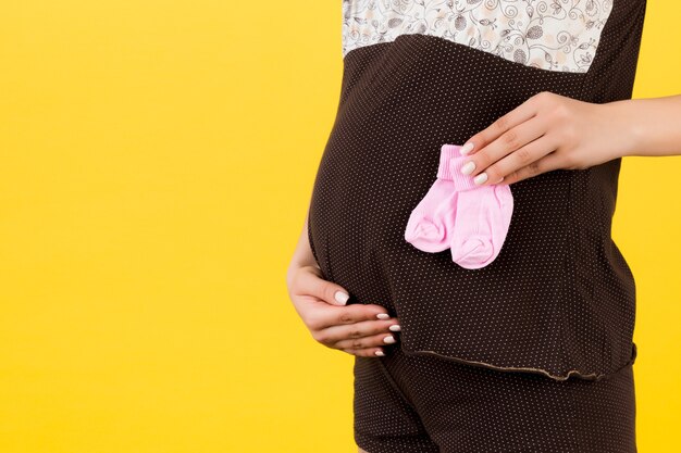 Close-up portret van zwangere vrouw in bruine pyjama met roze sokken voor een babymeisje op gele achtergrond. wachten op een kind. ruimte kopiëren.