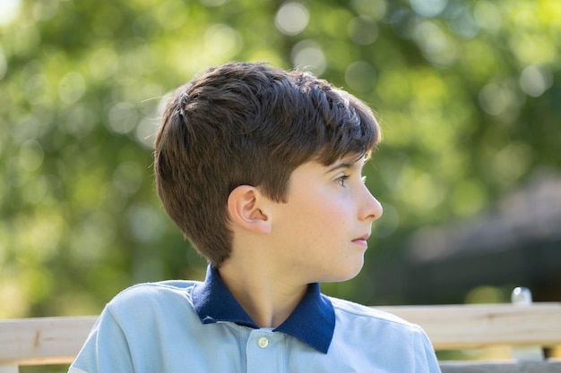 Close-up portret vooraanzicht van serieuze jonge jongen die wegkijkt zittend op een bank bokeh achtergrond