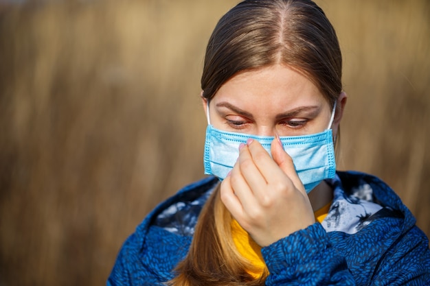 Close-up portret vrouw buiten in chirurgisch masker met rubberen oorbandjes. Typisch 3-laags chirurgisch masker om de mond en neus te bedekken. Proceduremasker van bacteriën. Beschermingsconcept.