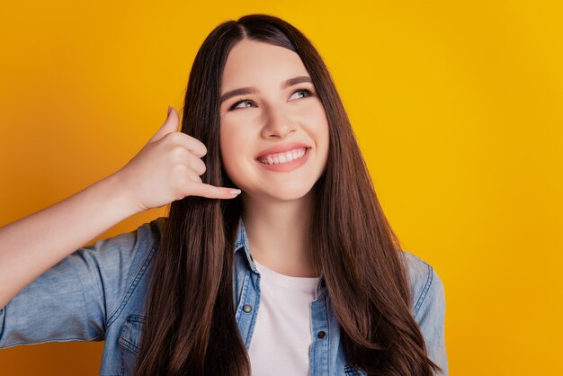 Close-up portret vrouw glimlachend vingers Toon bel me terug teken kijk lege ruimte geïsoleerde gele muur achtergrond