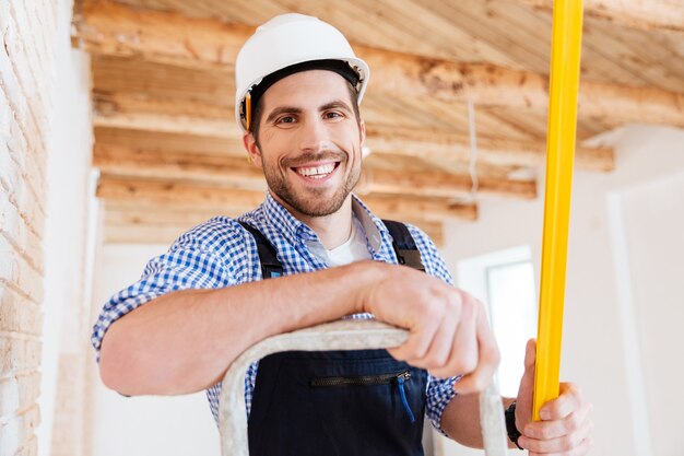 Close-up portrrait of a smilling handyman standing on the ladder with a level