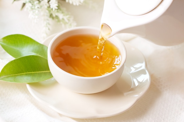 Close up pouring hot black tea in a white tea cup