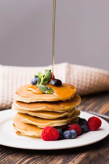 Close-up of pouring maple syrup on stack of pancakes.