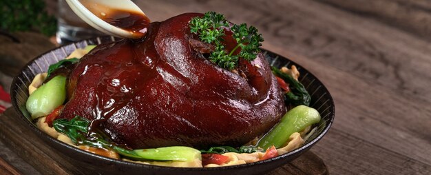 Close up of pouring savory soy sauce with spoon over Taiwanese food braised pork hock food in a plate on rustic table background.