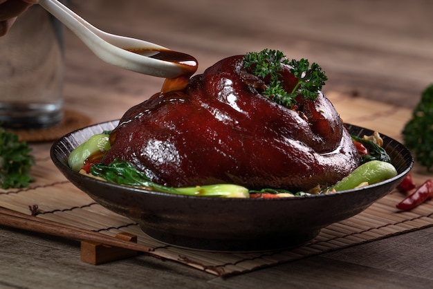 Close up of pouring savory soy sauce with spoon over Taiwanese food braised pork hock food in a plate on rustic table background.