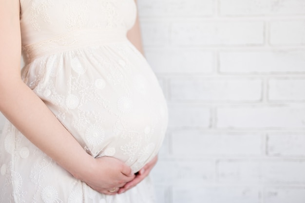 Close up of pregnant belly over white brick wall