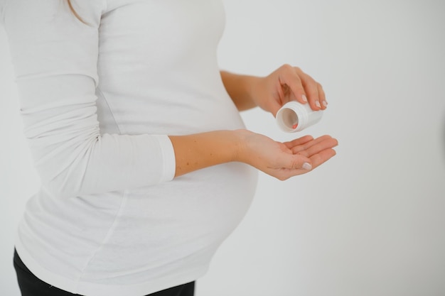 Primo piano sulla pancia incinta con la medicina... donna in attesa di un bambino vestito di pillole bianche in possesso. assunzione di farmaci o vitamine durante il concetto di gravidanza.